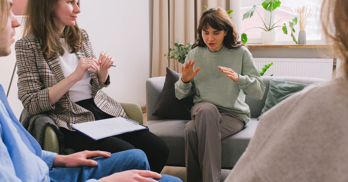 Women in casual clothes sitting on sofa and speaking during group psychotherapy session in cozy office